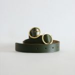 a green adjustable belt with brass hardware and fold logo