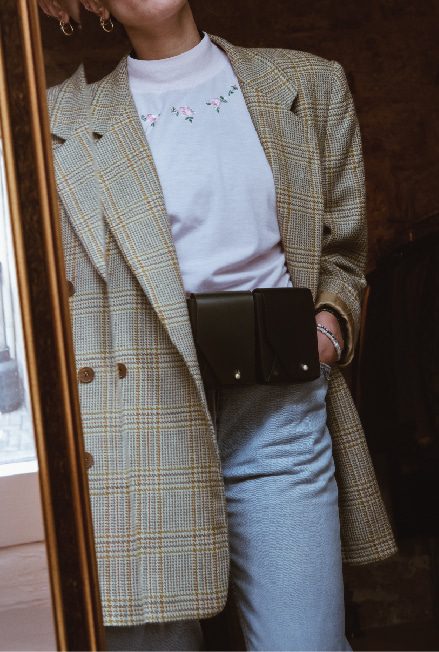 A woman wears a vintage tweed jacket, vintage mum jeans and two fold leather bags on one belt 