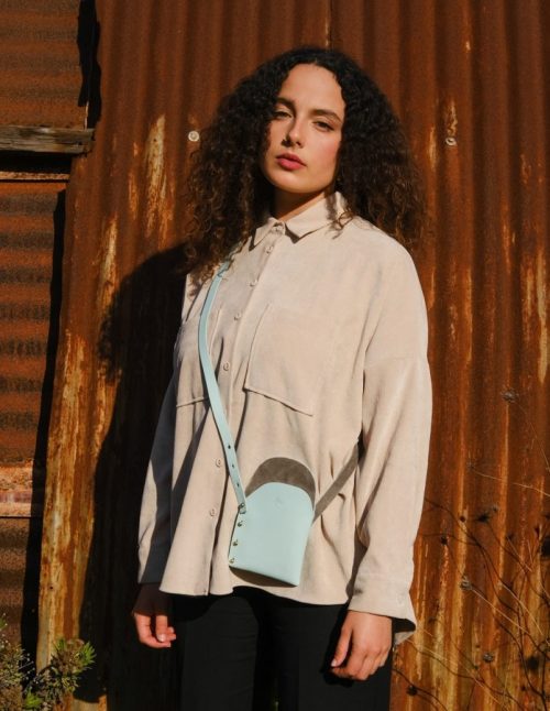 a female model wears a sky blue leather side bag across her body
