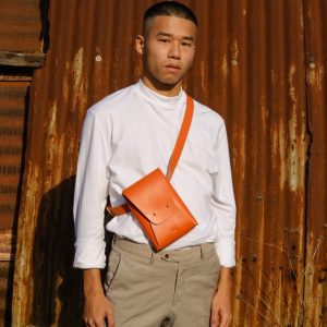 a male model wears an orange leather bag across his shoulders