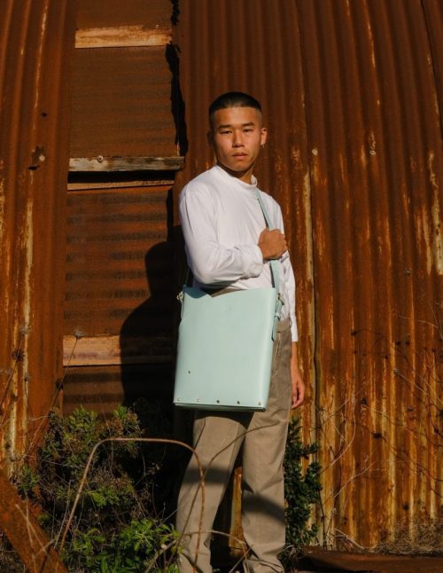 a male model wears a sky blue leather tote bag