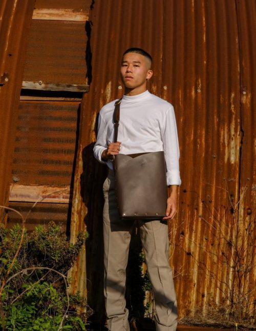 a male model wears a brown leather laptop bag